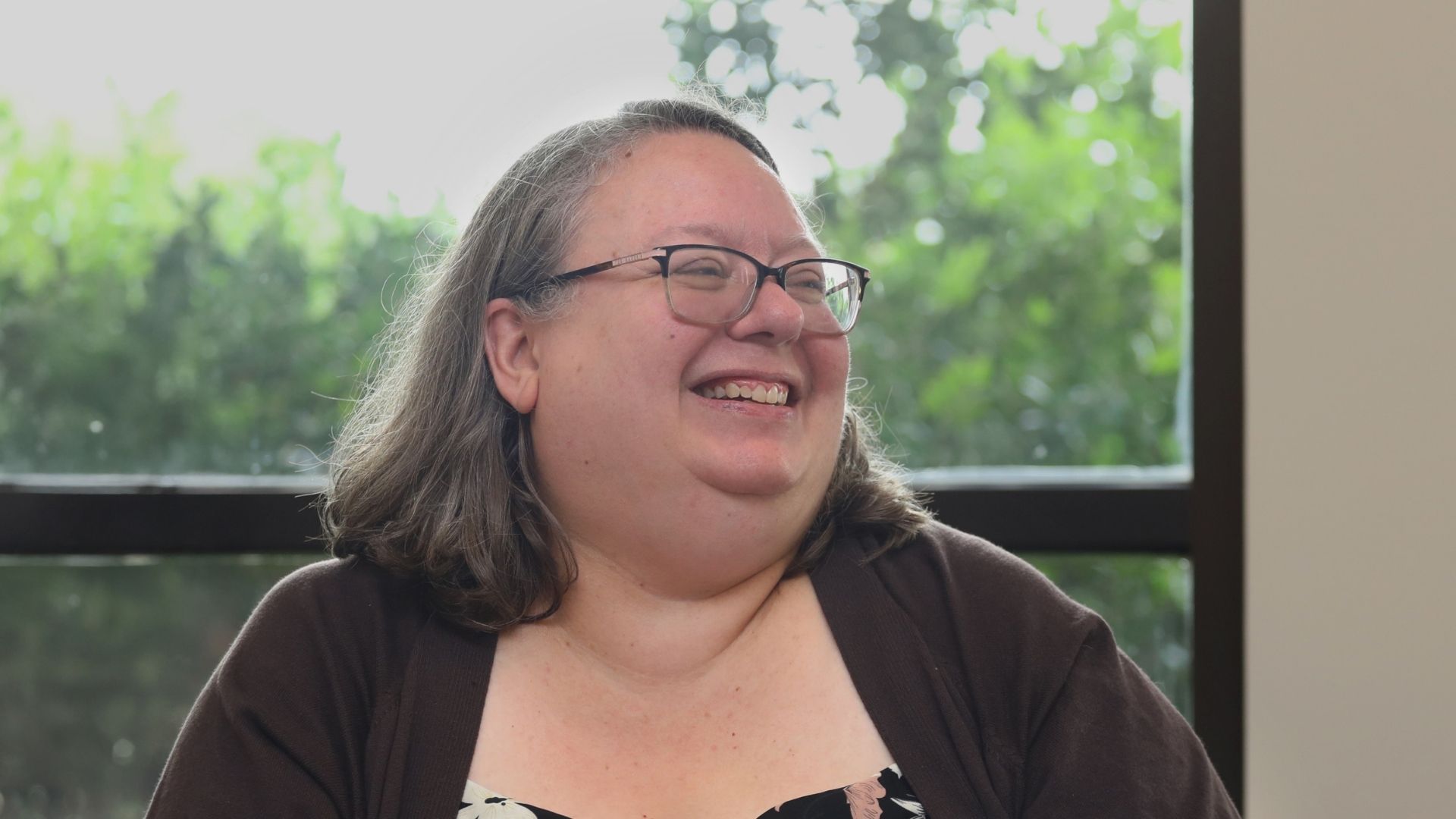 Headshot of Margaret Foster, smiling and looking off towards the right, a window with greenery behind her